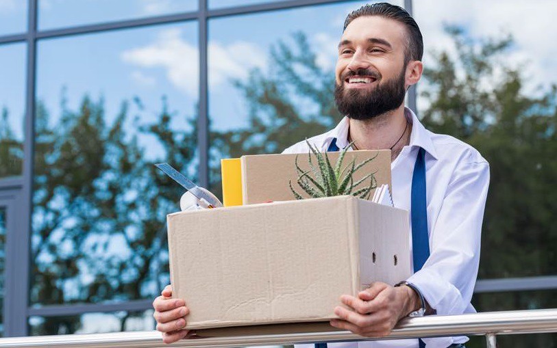 A man quitting job in front of the building with box of his stuff.